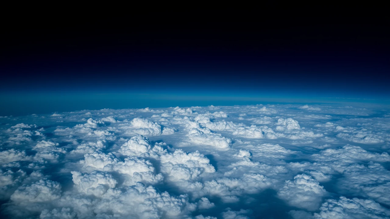 Wide view across a sea of cloud tops at blue hour, every crest rim lit in silver, the sky fading from dark navy overhead to bright blue at the horizon